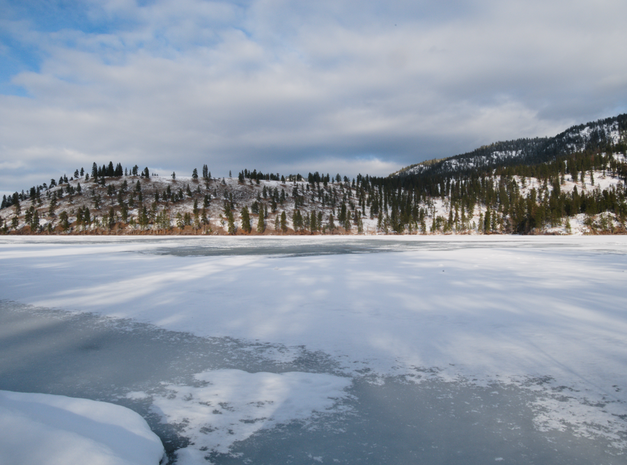 Vue sur le lac Kalamalka gelé avec des montagnes à l’arrière-plan.