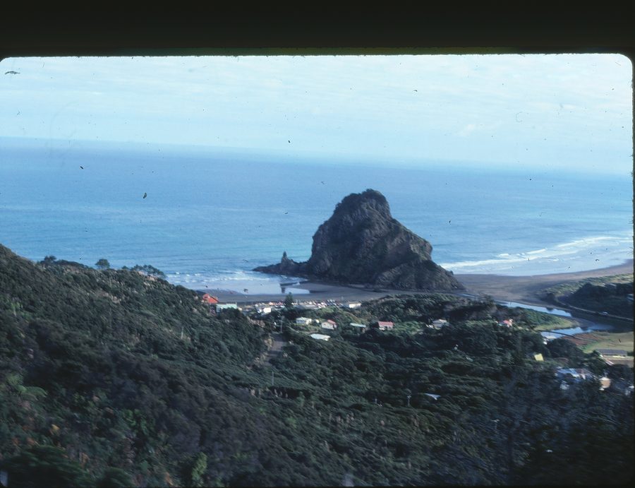 Plage de Piha avec sable noir, surf et caps rocheux.